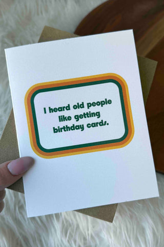 Hand holding a birthday card with humorous text on a soft surface