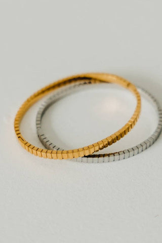 Two bracelets, one gold and one silver, on a light gray background