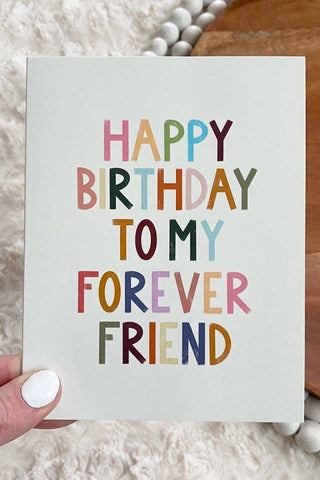 Hand holding a card with 'Happy Birthday to my forever friend' text on a textured surface.