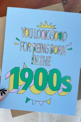 Card with humorous text 'You look good for being born in the 1900s' held by a hand.
