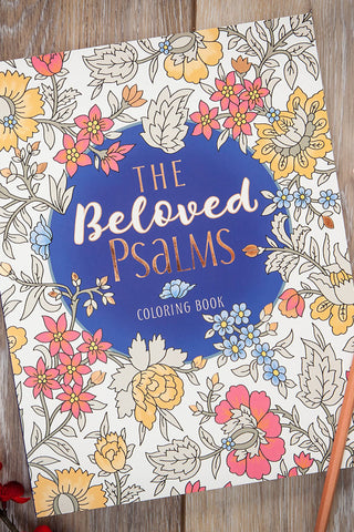 Coloring book titled 'The Beloved Psalms' on a wooden surface with flowers and candles.