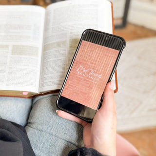 Person holding a phone with the Mod Threads app landing screen next to an open book on a wooden surface.
