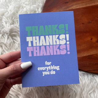Hand holding a blue card with 'THANKS! THANKS! THANKS!' text on a wooden surface.
