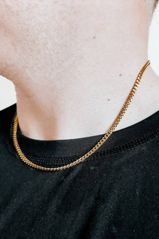 Person wearing a gold chain necklace on a plain background