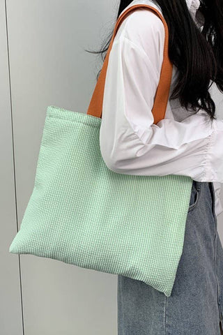 Person holding a green checkered bag against a plain background