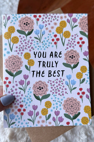 Card with floral design and text held by a hand on a textured surface