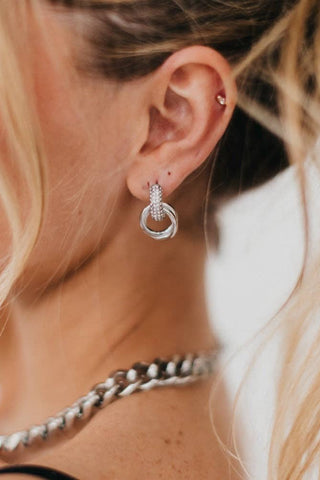 Close-up of a woman's ear wearing a silver hoop earring with a blurred background