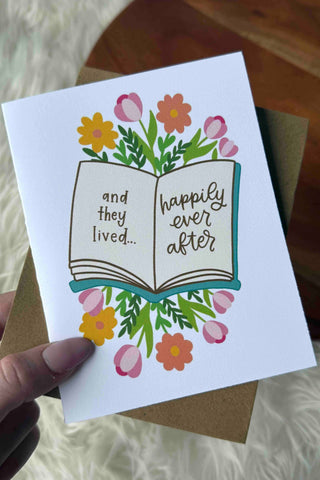 Greeting card with an open book illustration and floral design held by a hand.