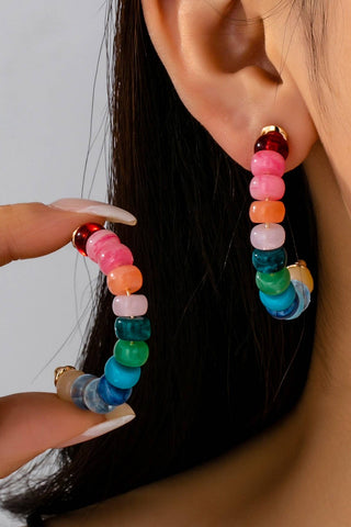 Multicolored beaded earrings being held up to an ear with a neutral background