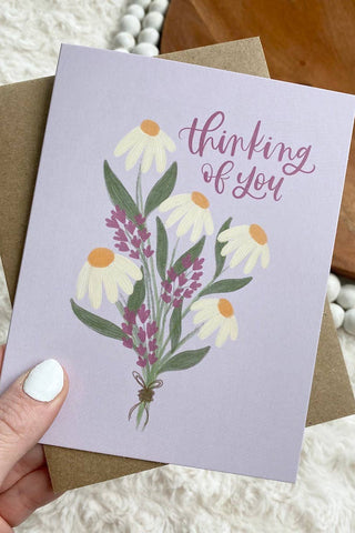 Greeting card with floral design and 'thinking of you' text held by a hand.