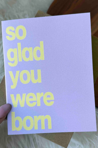 Hand holding a card with 'so glad you were born' text on a soft surface